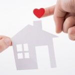 Paper house and  heart shape in hand on a white background
